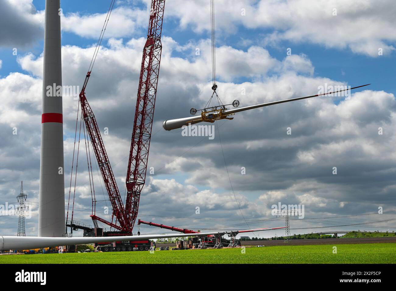 22 aprile 2024, Sassonia-Anhalt, Bad Lauchstädt: Una pala del rotore viene sollevata in aria da una gru per l'installazione su una turbina eolica nel parco energetico di Bad Lauchstädt. Il parco energetico di Bad Lauchstädt nella Germania centrale è attualmente il progetto pionieristico per l'idrogeno in Germania. In questo progetto di innovazione, la produzione di idrogeno verde da energia eolica, così come il suo stoccaggio, il trasporto, la commercializzazione e l'uso, sono stati testati su larga scala nella Germania centrale. Foto: Heiko Rebsch/dpa Foto Stock