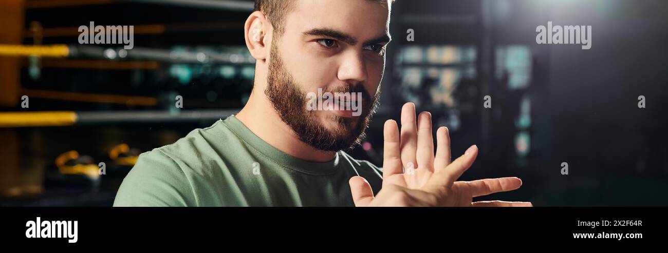 Un uomo con una camicia verde fa gesti attivamente, mostrando un segno di mano in una sessione di allenamento per autodifesa. Foto Stock