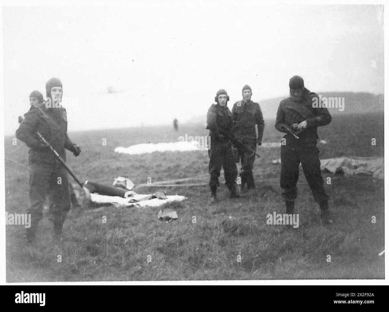Le truppe di paracadutisti raccolgono l'equipaggiamento dopo l'atterraggio durante operazioni su larga scala in Inghilterra, mentre un aereo da bombardamento in picchiata vola sopra la testa. Foto Stock