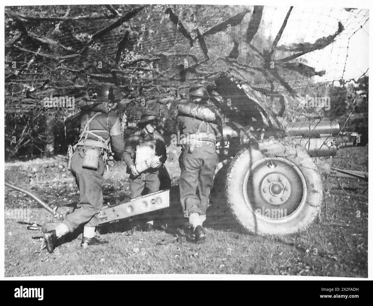 I cannoni caricano il loro cannone d'artiglieria, che è mimetizzato con reti per evitare l'osservazione aerea, durante l'addestramento di divisione in Scozia. Foto Stock