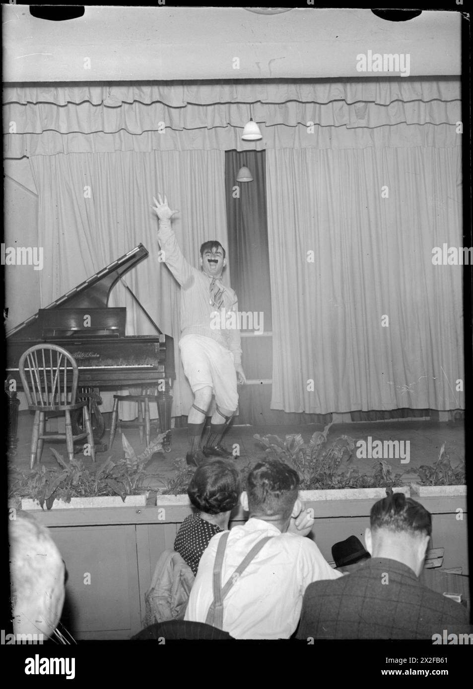 CARDIFF'S MERCHANT NAVY CLUB: REST AND RELAXATION IN CARDIFF, GLAMOURGANSHIRE, WALES, UK, c MAGGIO 1944 - Peter Kalfas è greco ed è un secondo ingegnere su una nave della marina mercantile britannica. Qui può essere visto mentre impersonava Hitler durante uno dei concerti del mercoledì sera tenuti regolarmente al Merchant Navy Club di Cardiff Foto Stock