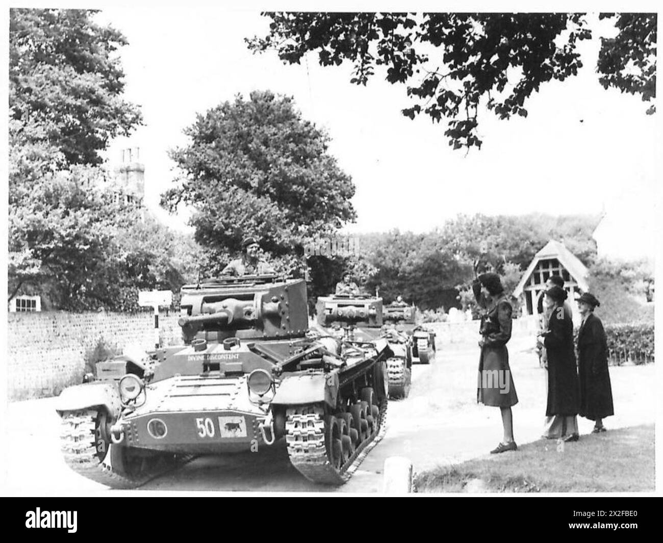 I carri armati Valentine si muovono attraverso un villaggio del Sussex mentre gli abitanti del villaggio locale osservano, mostrando il movimento militare all'interno delle aree civili durante gli esercizi. Foto Stock