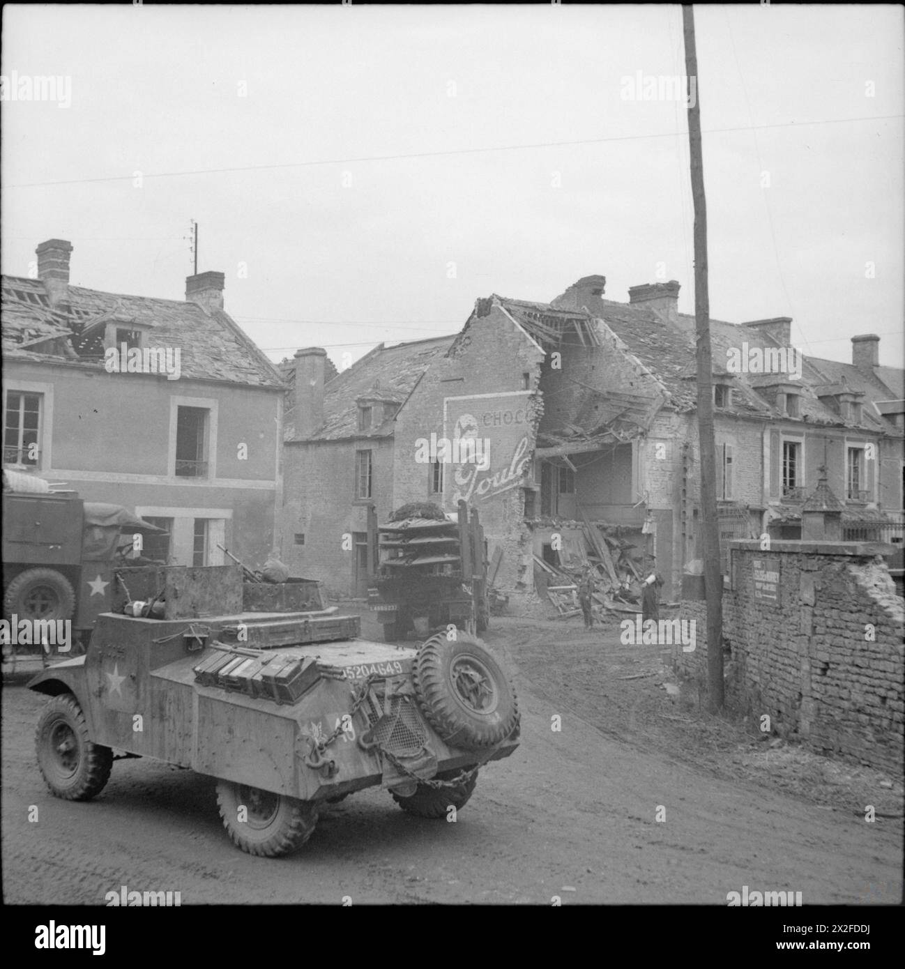 L'ESERCITO BRITANNICO IN NORMANDIA 1944 - Un'auto da ricognizione leggera Morris e altri veicoli che passano attraverso Bretteville, 30 giugno 1944 British Army Foto Stock