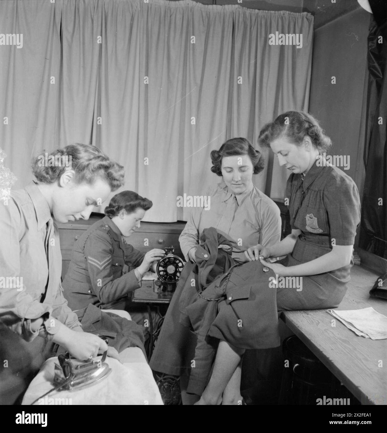 SERVICES CLUB: IL LAVORO DEL SERVIZIO VOLONTARIO FEMMINILE A CHESTER HOUSE, CLARENDON PLACE, LONDRA, INGHILTERRA, 1943 - le donne dell'ATS utilizzano la sala di lavoro del Services Club a Chester House. Il WVS fornisce ai membri del club una macchina da cucire, ferro elettrico e materiali per la rifinitura. Qui, Miss Albrecht (a destra), la supervisore del catering della filiale di Paddington della WVS, aiuta un membro dell'ATS a cucire un bottone sulla sua tunica Foto Stock