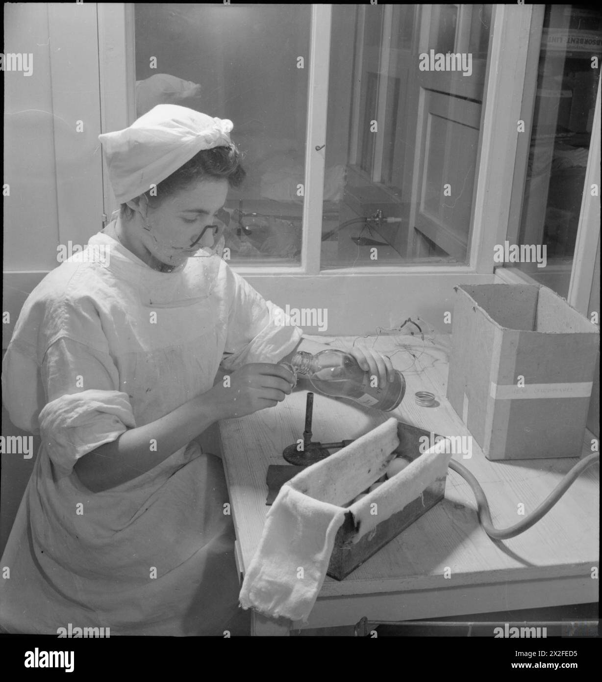 Un membro dello staff dell'unità di essiccazione del sangue dell'Università di Cambridge nel 1943 posiziona un coperchio su una bottiglia per trasfusione contenente plasma o siero sterile, utilizzando un tappo metallico perforato con cotone e muslin indossando una maschera protettiva. Foto Stock
