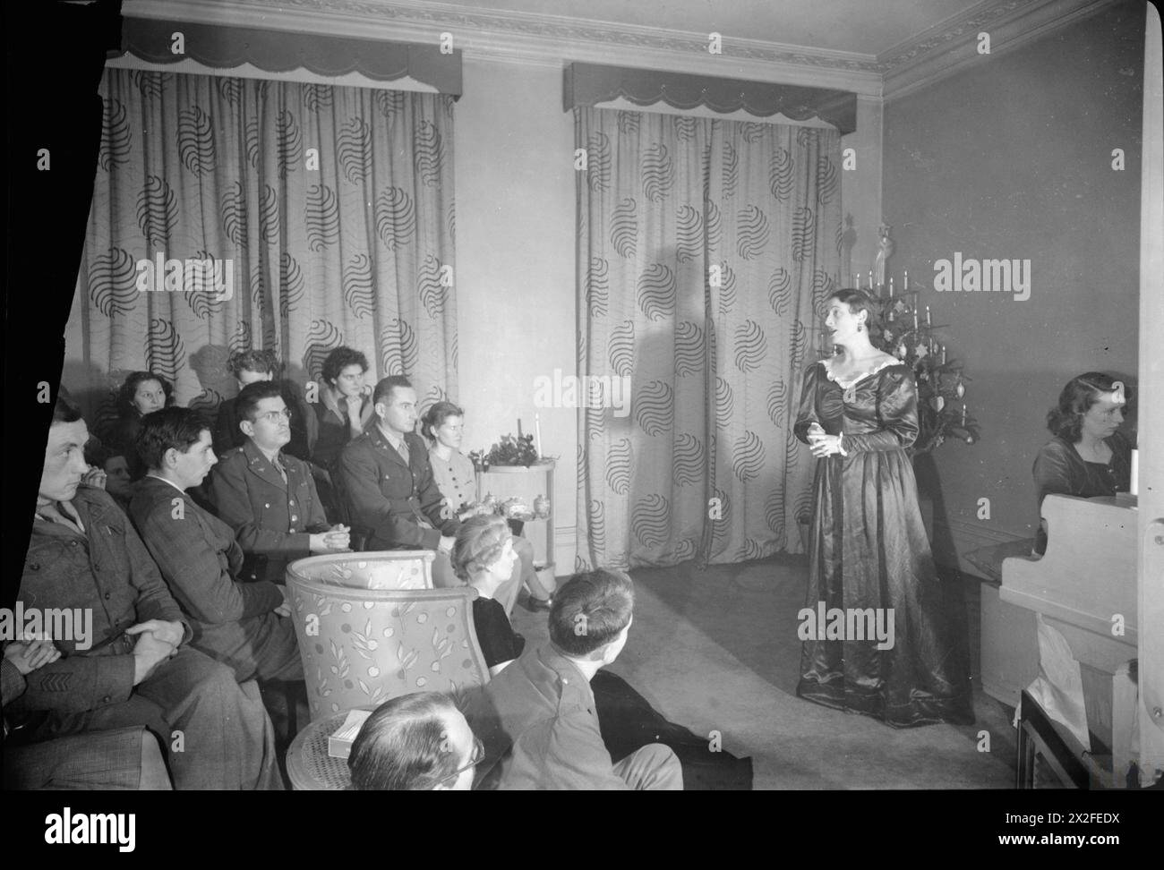 FESTA MUSICALE DI NATALE PER LE TRUPPE AMERICANE: CELEBRAZIONI A LONDRA, INGHILTERRA, Regno Unito, DICEMBRE 1944 - accompagnato da Dorothea Aspinall al pianoforte, il soprano Eve Maxwell Wright canta "i Saw Three Ships" in un piccolo concerto per le truppe americane in un appartamento a Buckingham Gate, Westminster. Un albero di Natale può essere visto nell'angolo, decorato con candele Foto Stock