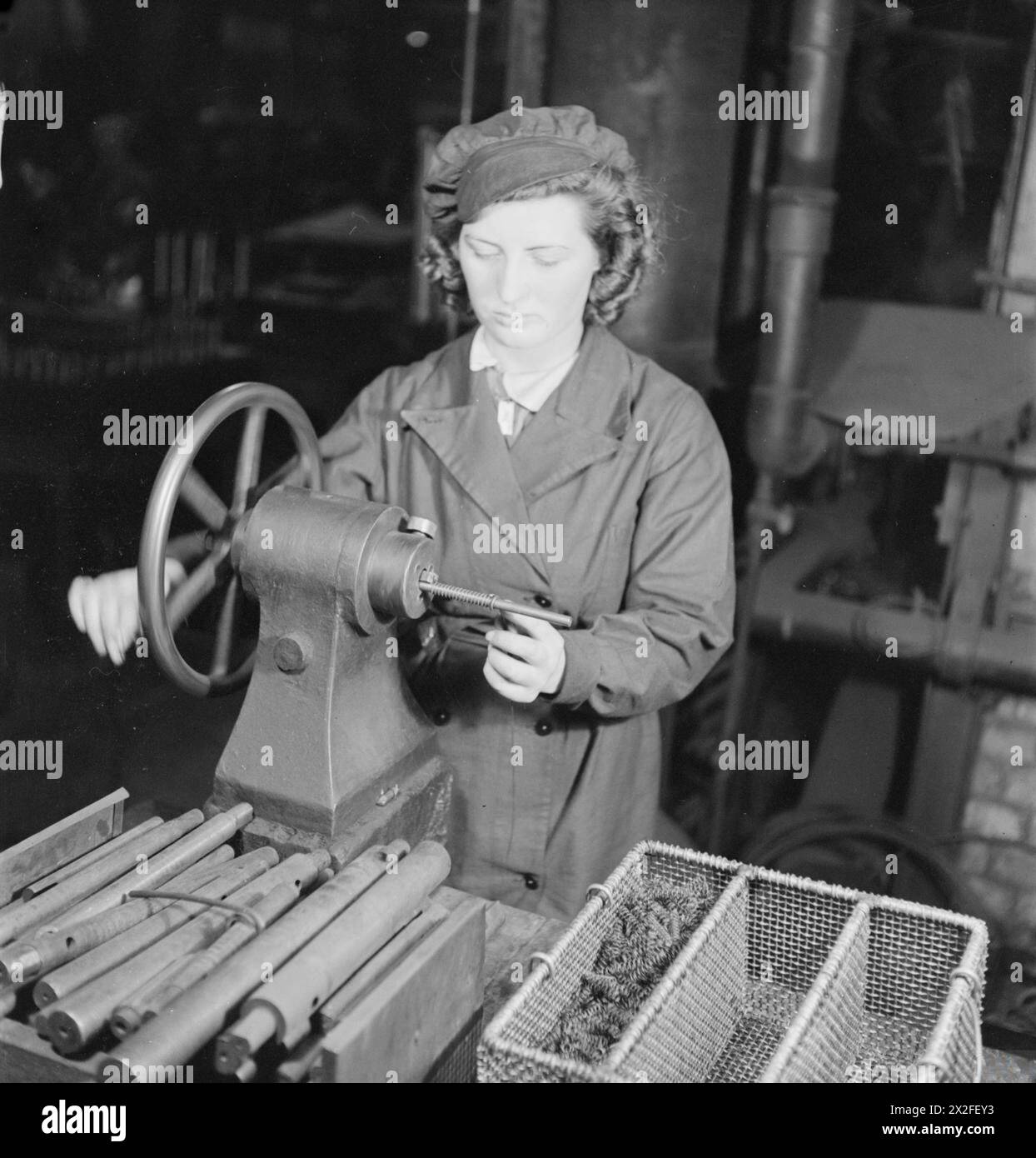 Una donna operatrice del metallo taglia e fa rotolare molle di compressione e di tensione, compresa una molla di tensione di mezzo pollice di diametro, per motori marini in Gran Bretagna durante la seconda guerra mondiale. Foto Stock