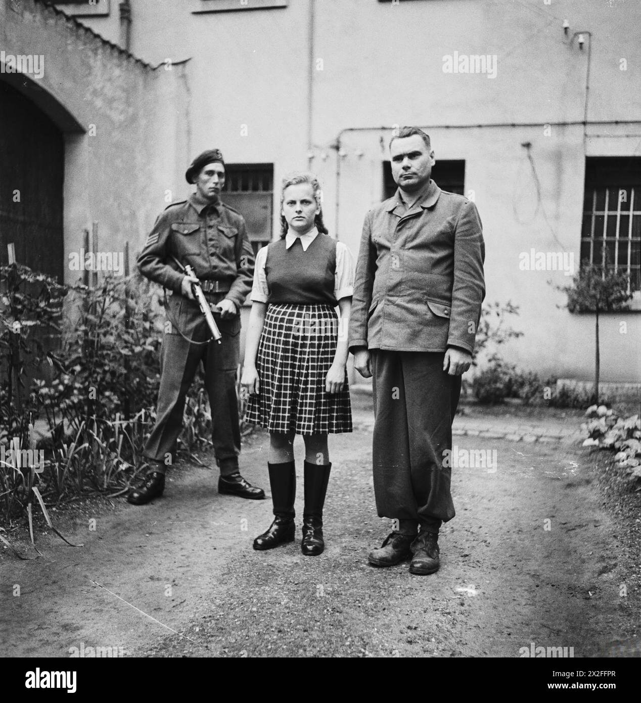 Irma Grese e Josef Kramer si trovano nel cortile della gabbia di prigionieri di guerra a celle in attesa di processo per crimini di guerra, agosto 1945, a seguito della liberazione del campo di concentramento di Bergen-Belsen. Foto Stock