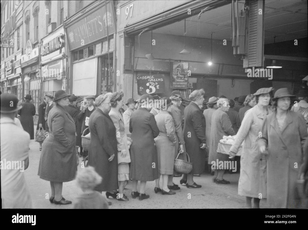 LA GRAN BRETAGNA FA LA FILA PER IL CIBO: RAZIONAMENTO E CARENZA DI CIBO IN TEMPO DI GUERRA, LONDRA, INGHILTERRA, Regno Unito, 1945 - donne e bambini fanno la fila fuori dal negozio del fruttivendolo di proprietà di J Wood, al 97-99 High Road, Wood Green, Londra. Sono visibili anche "B. Hemming" e "Hammett". Un segno nel greengrocer indica che i "verde cavolo" sono 3 1/2d per libbre Foto Stock