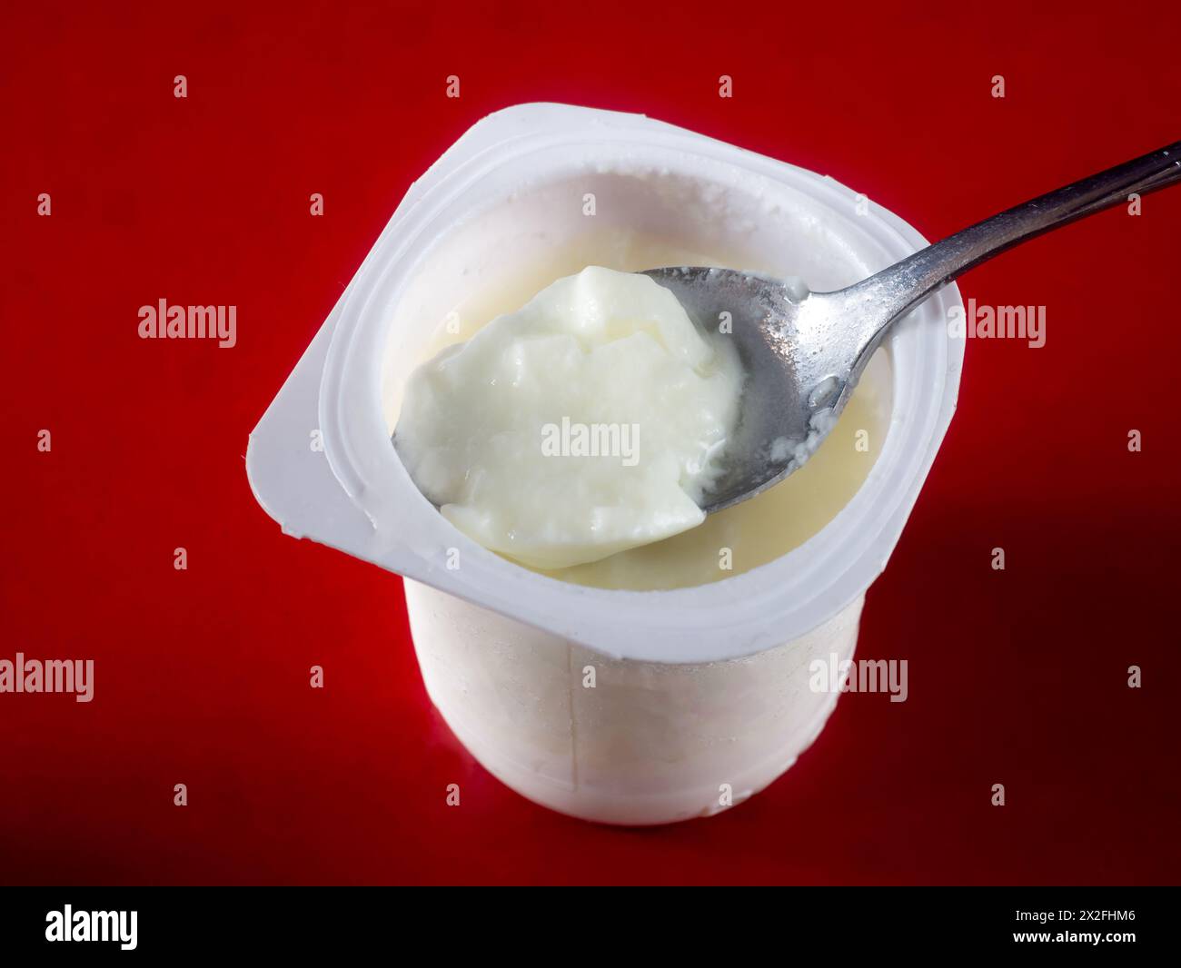 Tazza di yogurt con cucchiaio su sfondo rosso Foto Stock