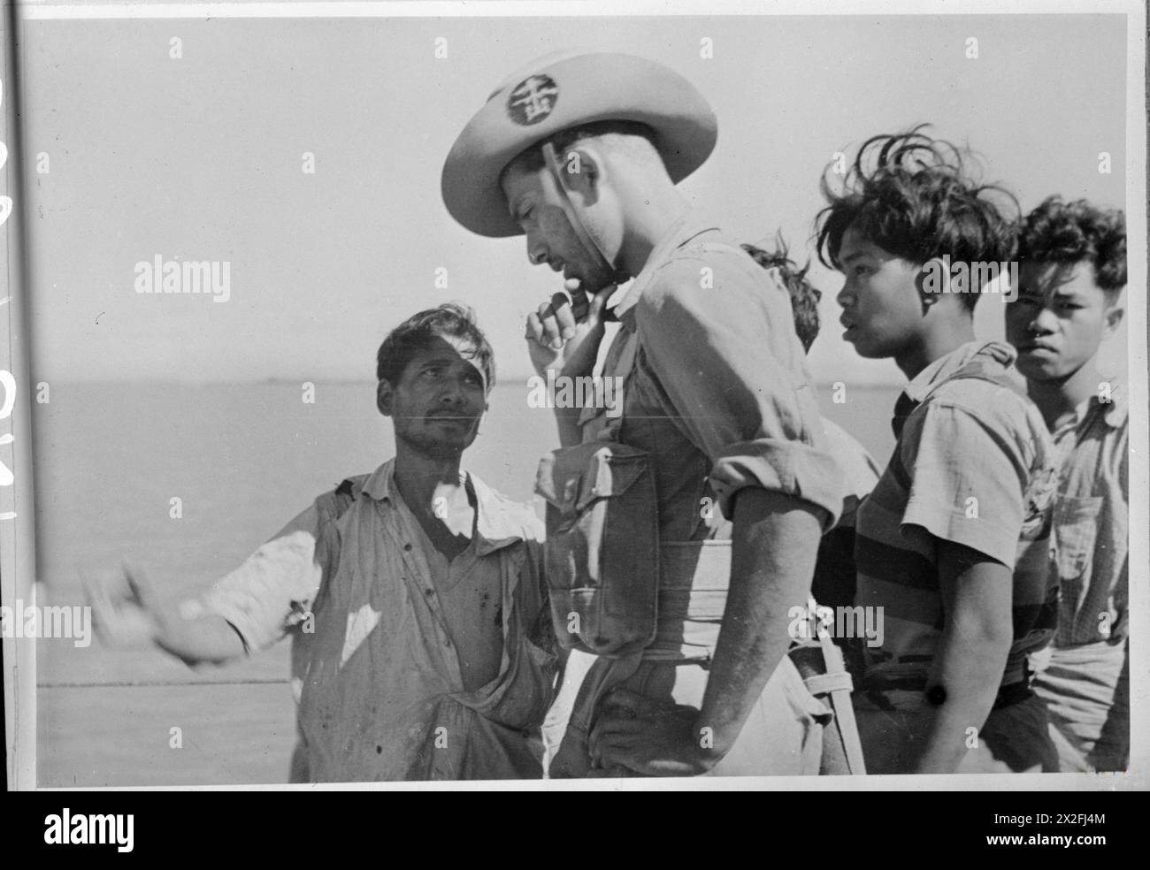 Forze britanniche, indiane e alleate cercano forze giapponesi via terra, mare e aria in Arakan. Un rating della Royal Indian Navy interroga gli abitanti del villaggio lungo il fiume Kaladan in Arakan. Foto Stock