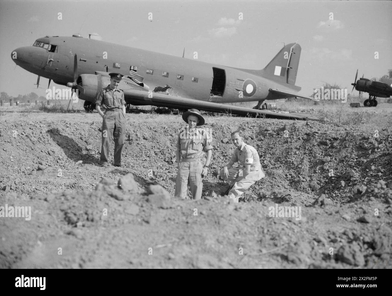 ROYAL AIR FORCE OPERATIONS IN THE ESTREMO ORIENTE, 1941-1945 - l'equipaggio del Douglas Dakota Mark III, KN232, del No. 238 Squadron RAF, (da sinistra a destra), Flying Officer J Creech (navigatore), Flight Lieutenant T J Bayliss (pilota) e Leading Aircraftman i Fiddes (infermiere), in un cratere bombardato dal loro aereo danneggiato dopo che è stato bombardato dai giapponesi prima di decollare a Meiktila, Birmania. (Cfr. Informazioni supplementari) Royal Air Force, Group, 238 Foto Stock