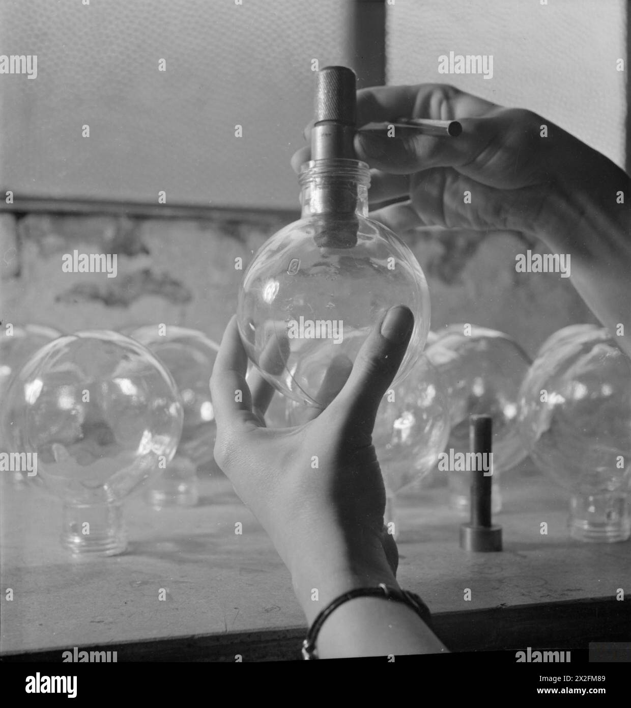 Un pallone di vetro viene esaminato in una fabbrica britannica che produce No. 74 bombe adesive nel 1943. I matracci costituiscono il corpo principale della bomba e sono rivestiti di adesivo e involucro protettivo prima di essere riempiti di esplosivi in un impianto di riempimento. Foto Stock