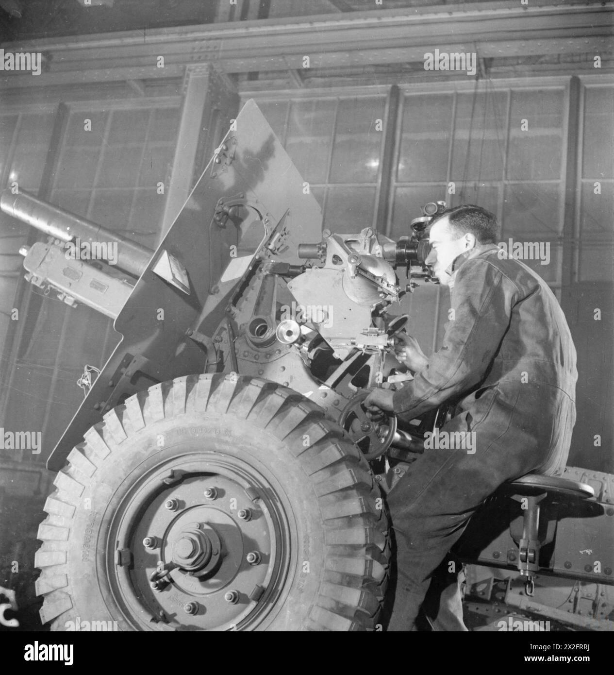 NASCITA DI Un CANNONE: LA PRODUZIONE DI Un CANNONE da CAMPO DA 25 POUNDER, 1942 - il cannone da 25 libbre completamente equipaggiato è testato per la precisione, sia in orizzontale che in verticale, su un bersaglio appositamente fissato alla fine dell'officina. L'operaio della fabbrica, il signor Redfern, controlla e testa la visuale della pistola Foto Stock