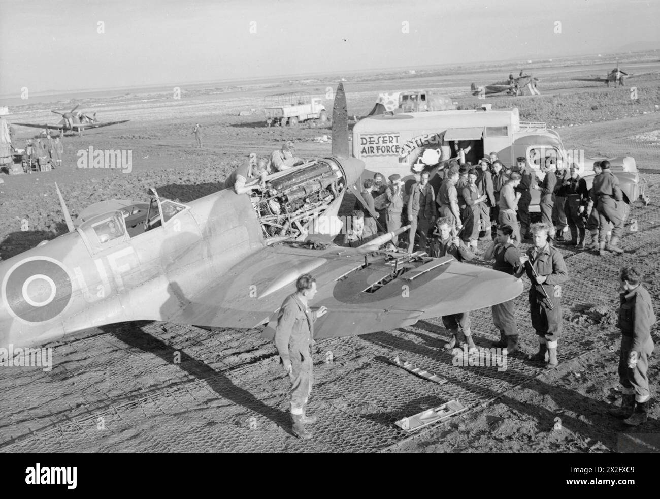 ROYAL AIR FORCE: ITALIA, BALCANI ED EUROPA SUDORIENTALE, 1942-1945. - L'equipaggio di terra del No. 244 Wing RAF ottiene rinfreschi da una mensa mobile della Desert Air Force in un disperso a Canne, Italia, mentre, in primo piano, continua la manutenzione su un Supermarine Spitfire Mark VC del No. 601 Squadron RAF. La mensa fu presentata alla RAF dal famoso Alexandrian, barone Charles de Menasce, Royal Air Force, 244 Wing, Royal Air Force, Expeditionary Air Wing, 140, Royal Air Force, Air Force, Western Desert Foto Stock