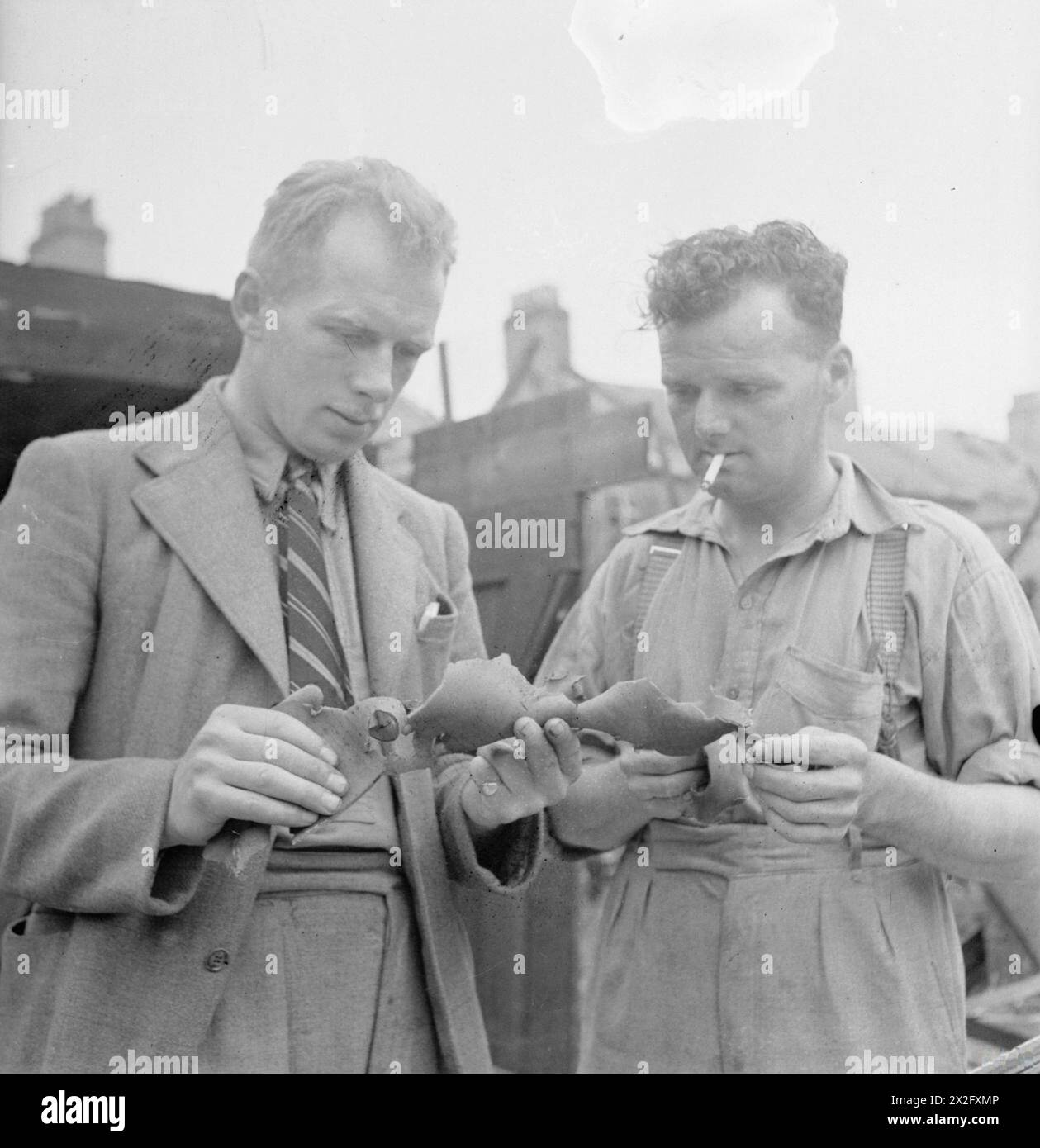 CAMPO DI LONDRA DELLA SQUADRA DI RIPARAZIONE BLITZ: LA VITA DI TUTTI I GIORNI CON LE SQUADRE DI RIPARAZIONE BLITZ, LONDRA, INGHILTERRA, Regno Unito, 1944 - il generale Foreman J Wigley (di Darlington) e il CAPOSQUADRA H Uttley esaminano un pezzo dei resti di una bomba volante V1. Fanno parte di una squadra di costruttori che sono venuti a Londra da varie parti del paese per riparare i danni causati da queste bombe Foto Stock