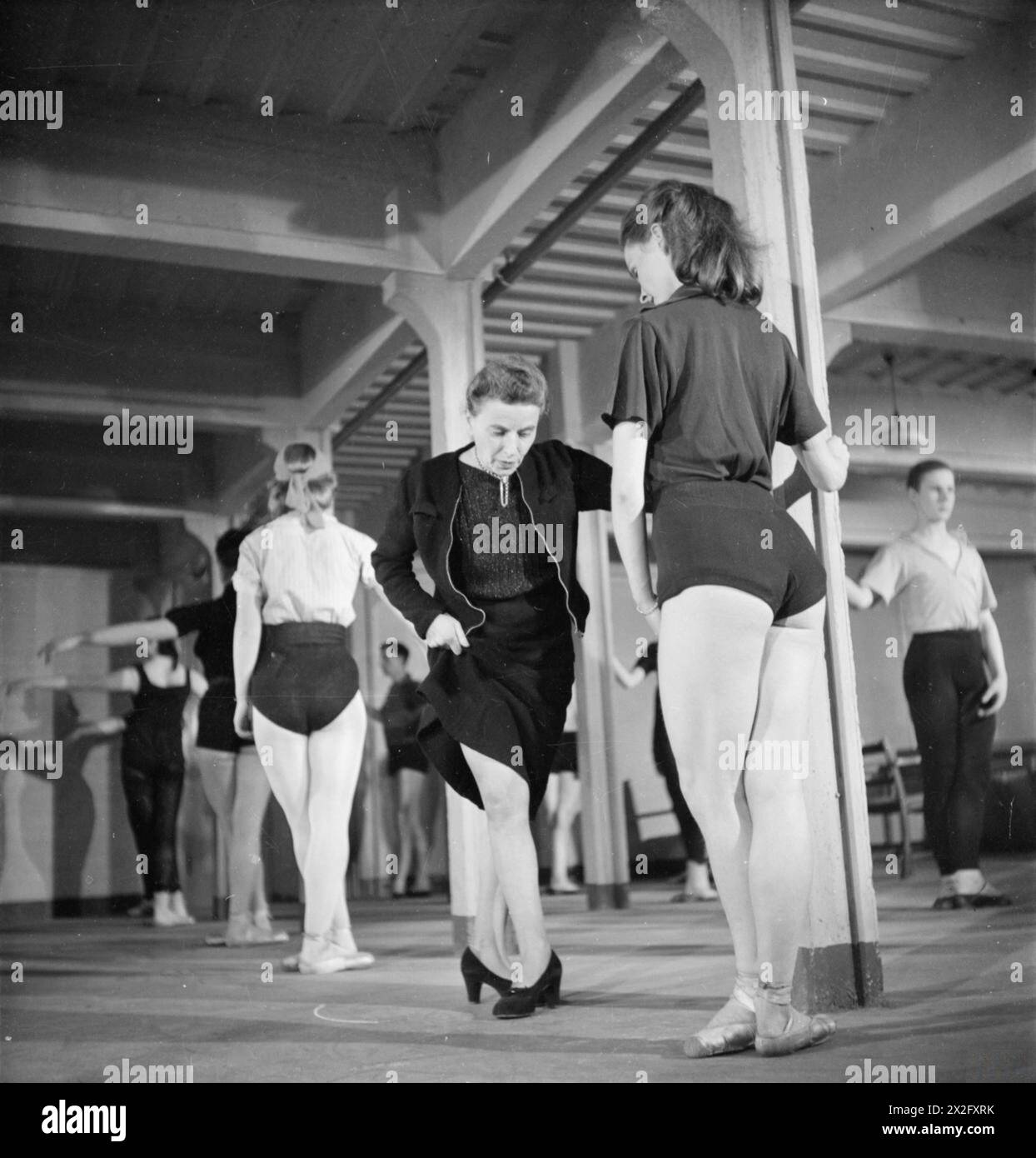 IL BALLETTO VA ALLA FABBRICA: DANZA E INTRATTENIMENTO ORGANIZZATO DAL COUNCIL FOR THE ENCOURAGEMENT OF MUSIC AND THE ARTS, INGHILTERRA, 1943 - Marie Rambert (centro), fondatrice e direttrice del Ballet Rambert, dimostra un nuovo passo verso la ballerina Sally Gilmour, durante una prova nella sala giochi dell'ostello della fabbrica. Questa prova si svolge al mattino, mentre i lavoratori della fabbrica sono impegnati nel loro lavoro Foto Stock