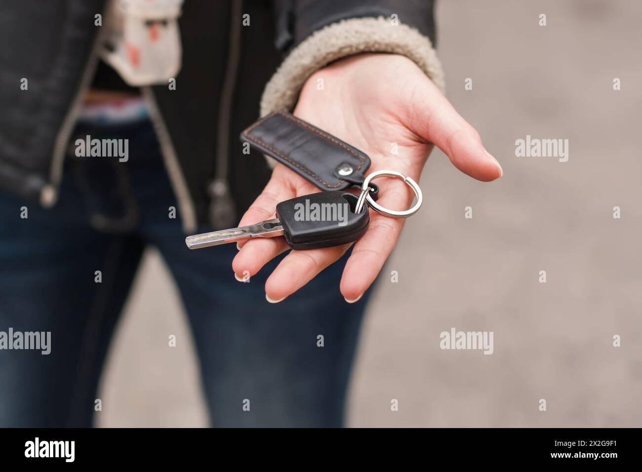 Trasferimento delle chiavi dell'auto in mano femminile, giacca nera Foto Stock