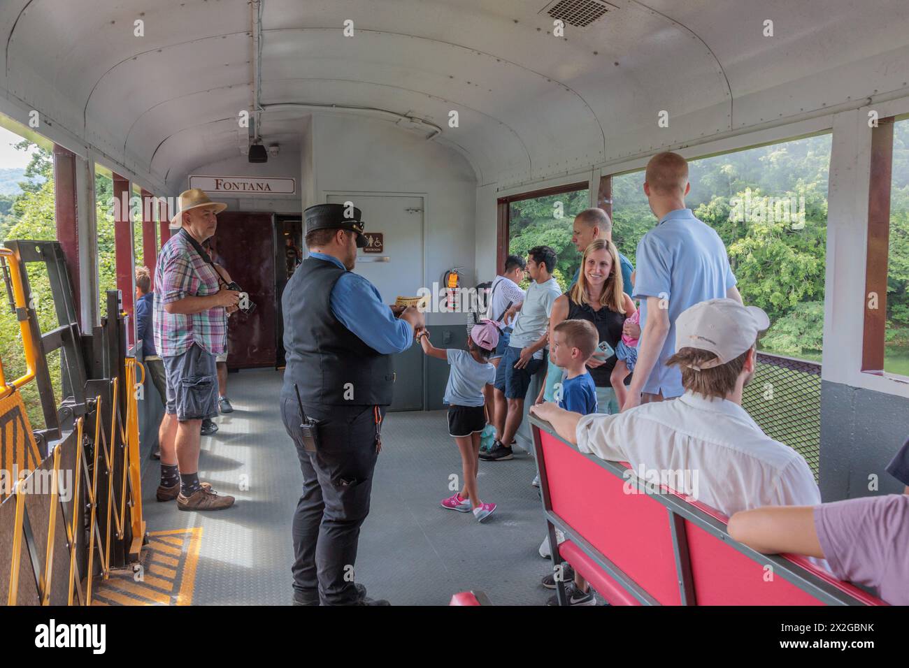 La giovane famiglia guarda un collezionista di biglietti prendere a pugni i loro biglietti ricordo durante l'escursione alla ferrovia delle Great Smoky Mountains da Bryson City, North Carolina Foto Stock