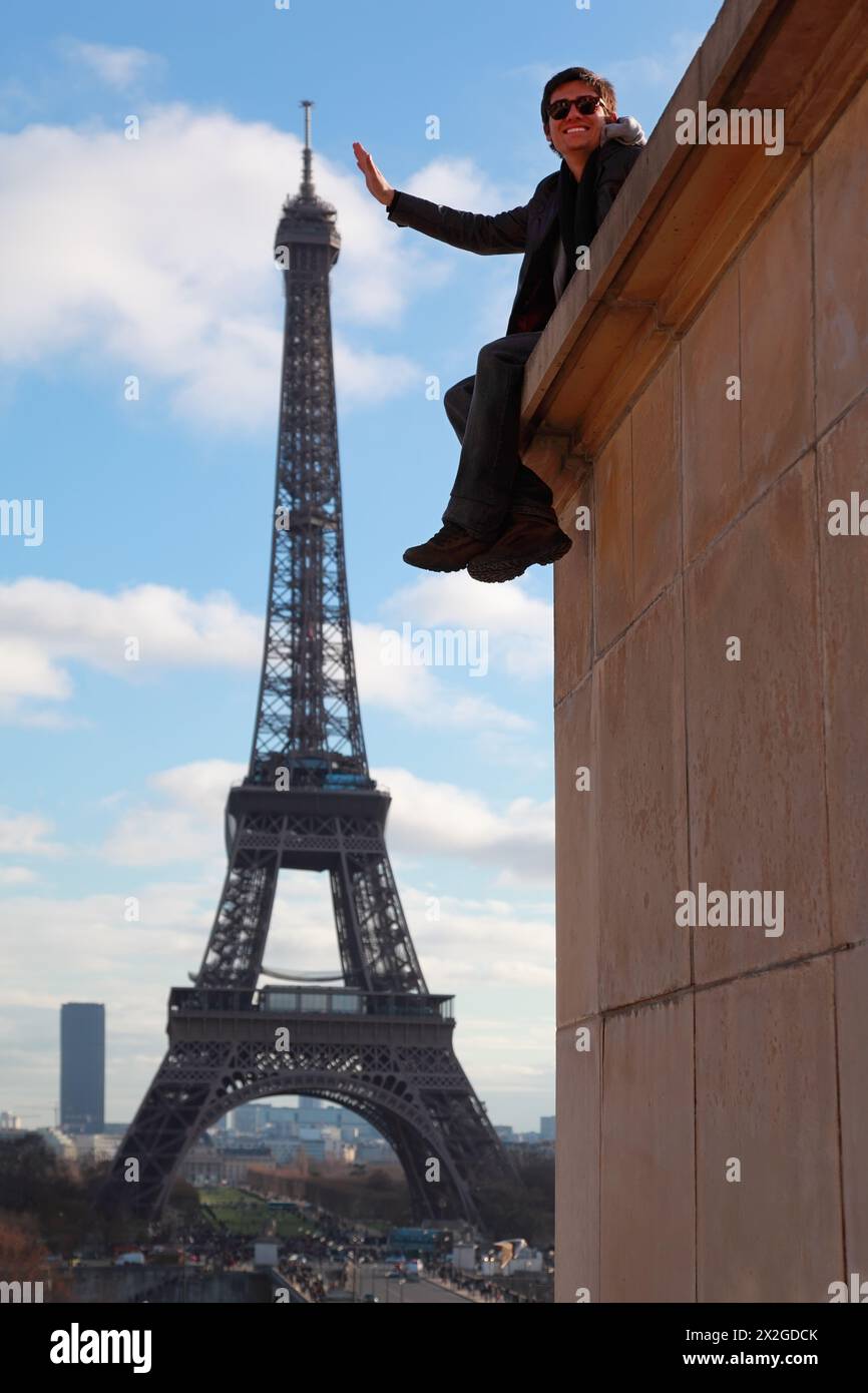 PARIGI - 2 GENNAIO: Uomo con occhiali da sole seduto sul muro, posa, fingendo che tocchi la Torre Eiffel il 2 gennaio 2010 a Parigi. Peso della Torre Eiffel Foto Stock