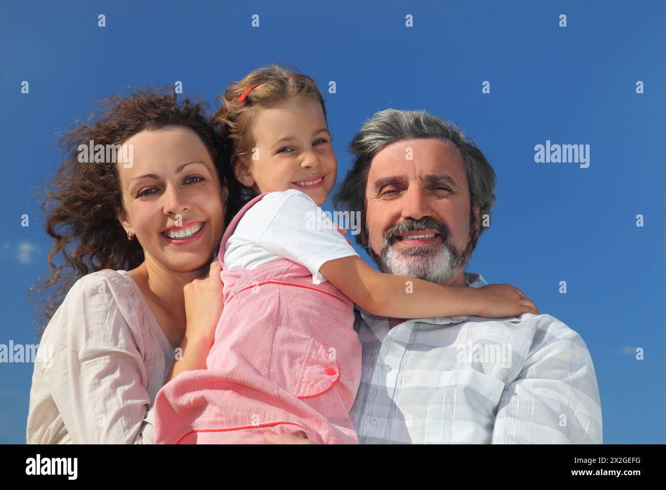 famiglia con ragazza, madre e nonno sorridenti e avvolgenti, cielo blu Foto Stock