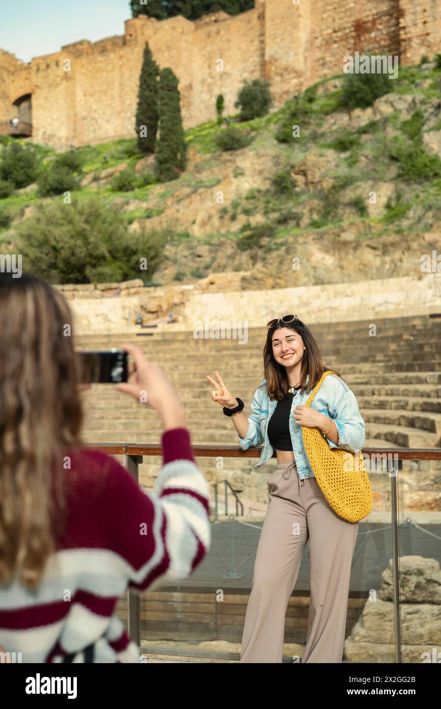 Una ragazza, una turista, con le spalle alla telecamera, cattura con gioia la sua amica mentre posa di fronte a un monumento. Foto Stock