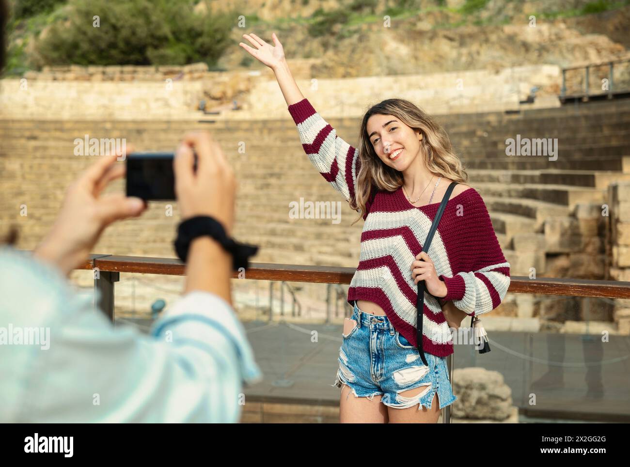 Due amici turisti si posano di fronte a un monumento a Malaga, mentre uno fotografa l'altro sorridendo e sollevando un braccio. Foto Stock