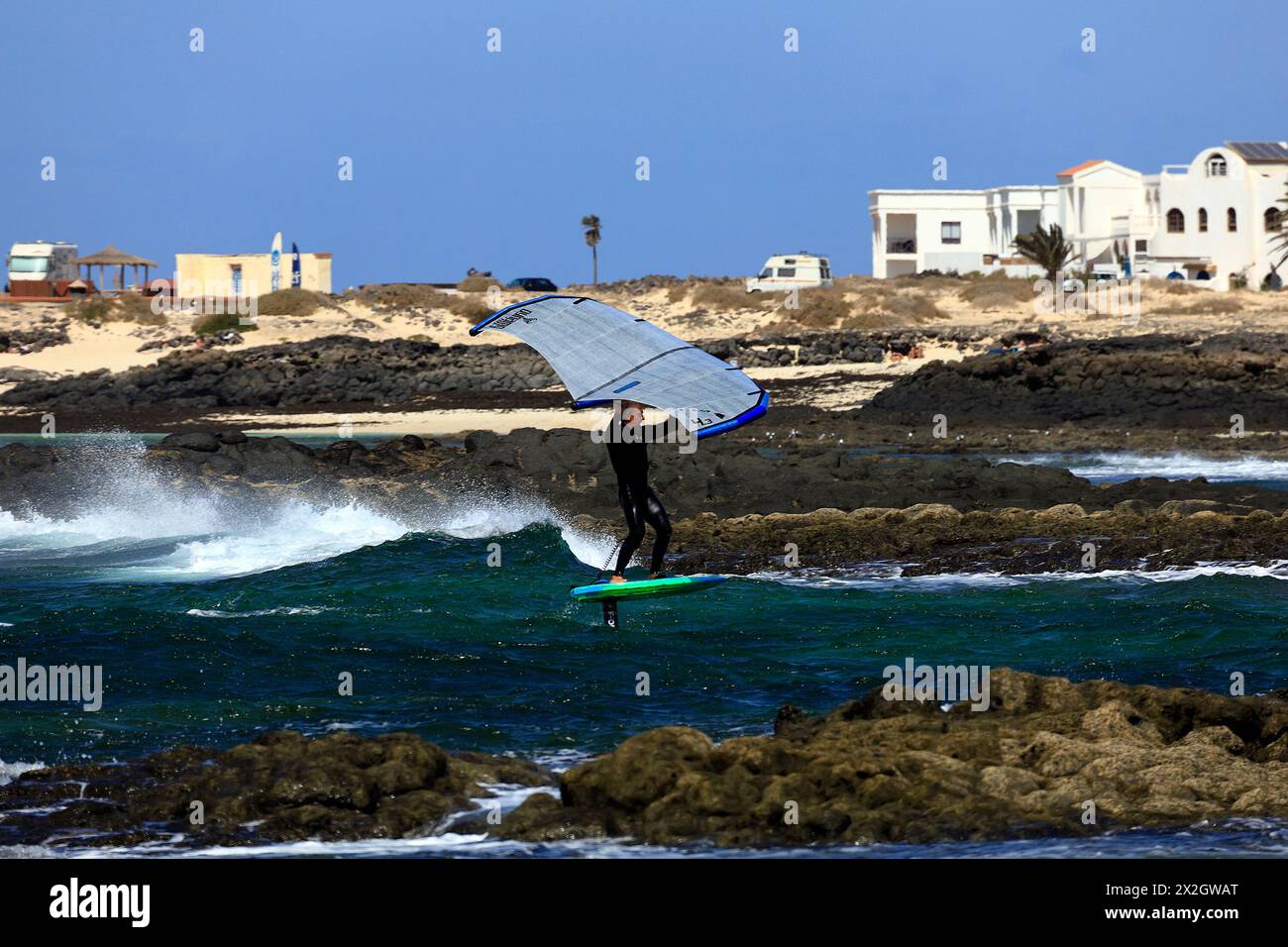 Fai surf con una tavola da surf con lama d'aliscafo subacquea, affrontando la costa rocciosa in mare accidentato. El Cotillo, Fuerteventura. Febbraio 2024 Foto Stock