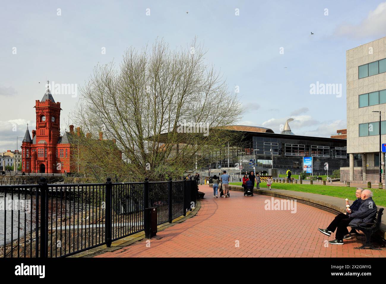 Cardiff Bay con Pierhead Building e Assembly Building e una coppia di anziani su una panchina che si gode 99 coni di gelato. Preso nell'aprile 2024 Foto Stock