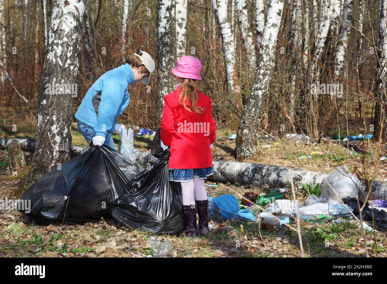 Il retro del fratello e della sorella con borse nere raccolgono la spazzatura dell'anno scorso al parco in primavera Foto Stock