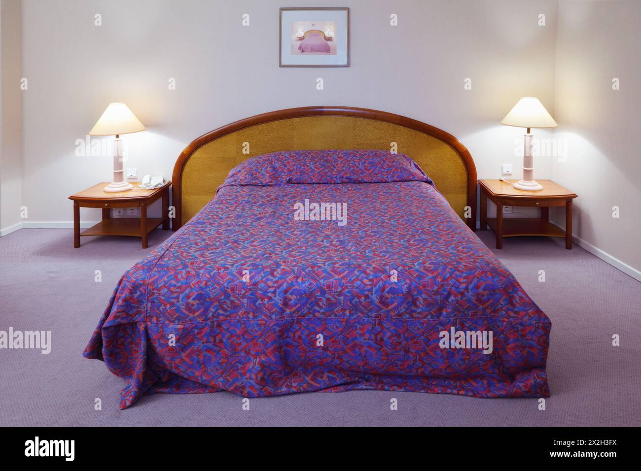 Camera semplice, luminosa e confortevole in hotel; grande letto e due comodini con lampade Foto Stock