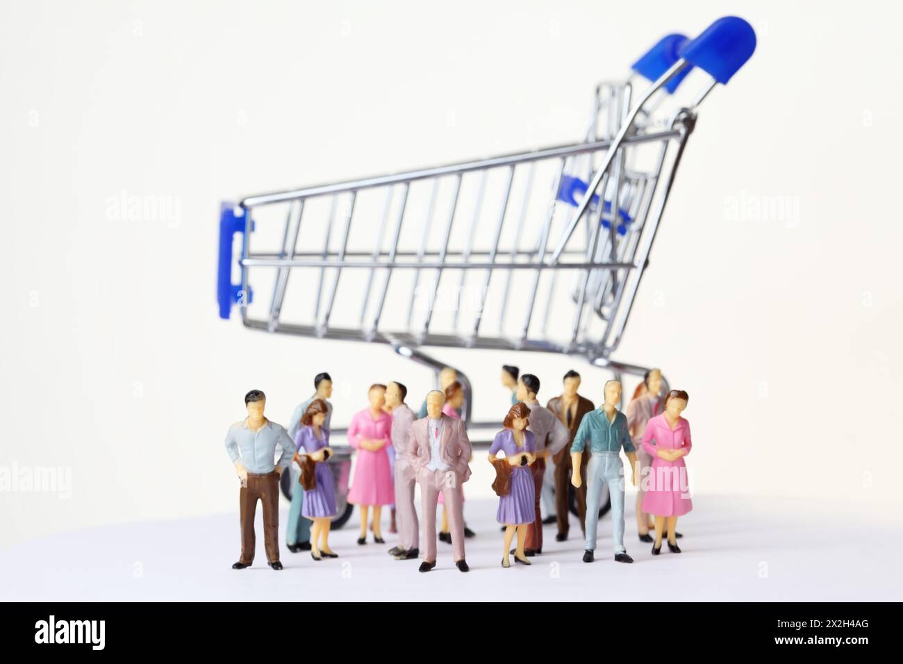 le persone dei giocattoli in miniatura multicolore si trovano in posizioni diverse vicino al grande carrello della spesa Foto Stock