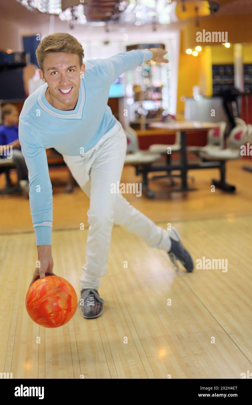 Il giovane uomo sorridente che indossa un maglione blu lancia la palla nel bowling; bassa profondità di campo Foto Stock