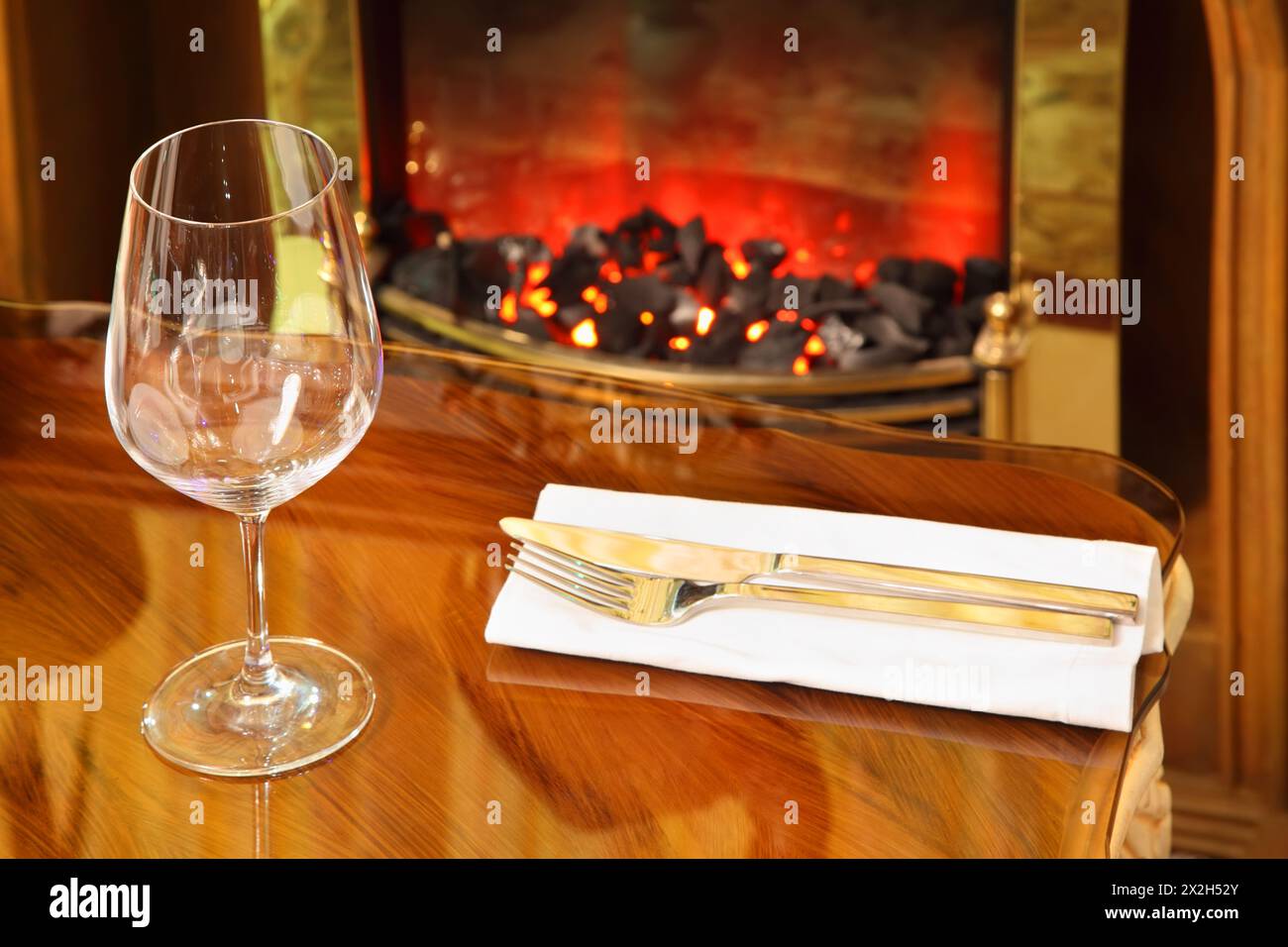svuotare il bicchiere, il coltello e la forchetta su un tovagliolo bianco al tavolo del ristorante; i carboni si mescolano nel caminetto Foto Stock