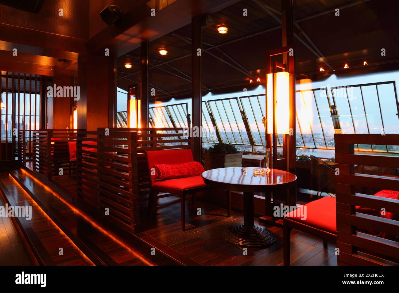 Fila di tavoli marroni e posti a sedere rossi con pareti divisorie in un intimo ristorante vuoto la sera Foto Stock