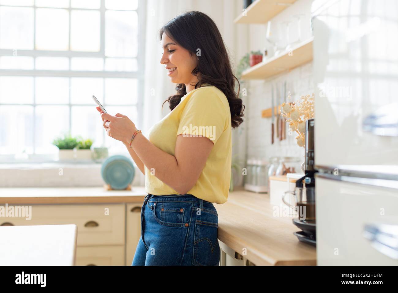 Donna che controlla il telefono in una cucina soleggiata Foto Stock