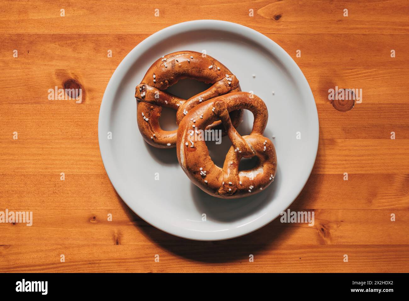 Vista dall'alto di due pretzel appena sfornati su un piatto su un tavolo di legno Foto Stock