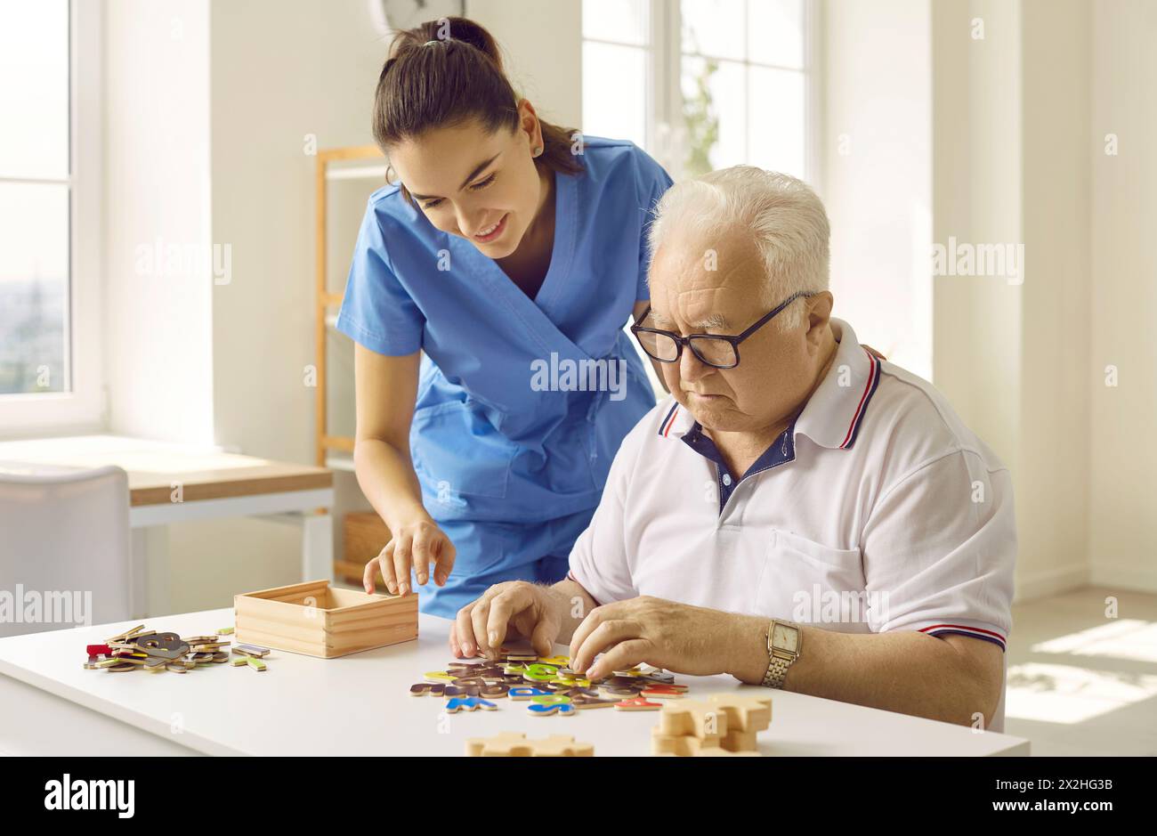 Infermiere o infermiere in una casa di riposo che aiuta un anziano demente con enigmi Foto Stock