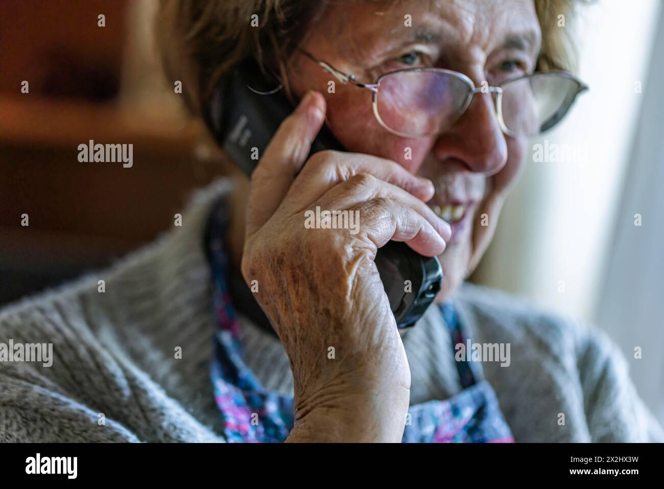 Una anziana cittadina sembra seria, spaventata mentre parla al telefono nel suo salotto, Colonia, Renania settentrionale-Vestfalia, Germania Foto Stock