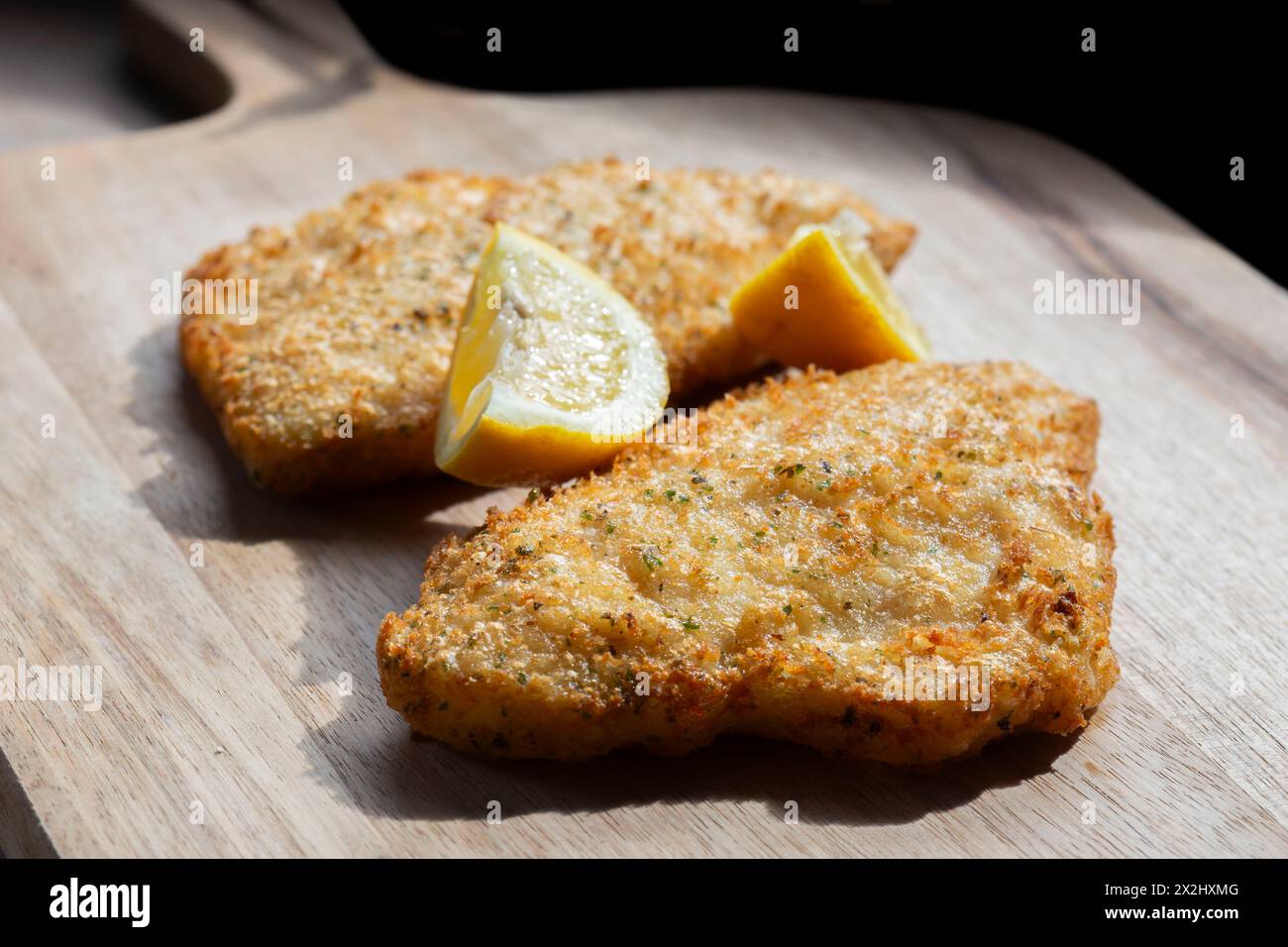 Filetti di merluzzo in pastella tempura ricoperti di erbe aromatiche e limone con una fetta di limone. Su un tagliere di legno. Foto Stock