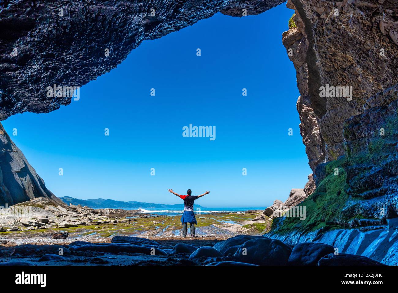 Uomo escursionista nella grotta marina della baia di Algorri sulla costa flysch di Zumaia, Gipuzkoa. Paesi Baschi Foto Stock