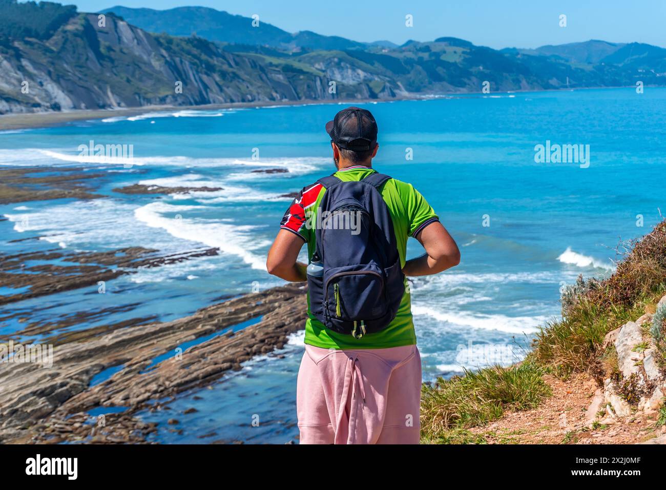 Un uomo con la schiena si è girato nella baia di Algorri sulla costa nel flysch di Zumaia, Gipuzkoa. Paesi Baschi Foto Stock