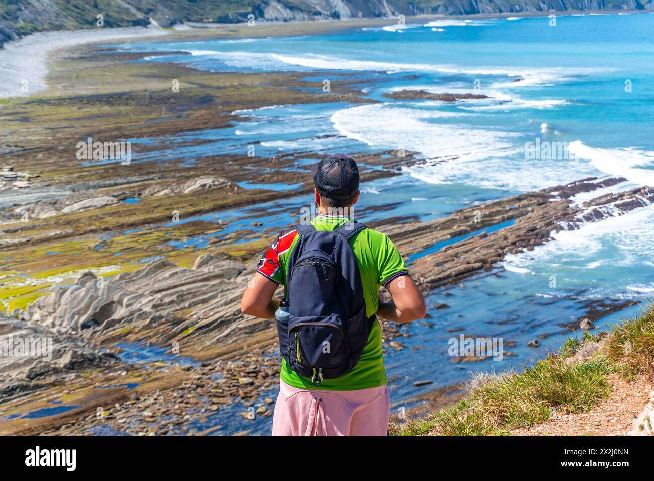 Un uomo con la schiena si è girato nella baia di Algorri sulla costa nel flysch di Zumaia, Gipuzkoa. Paesi Baschi Foto Stock