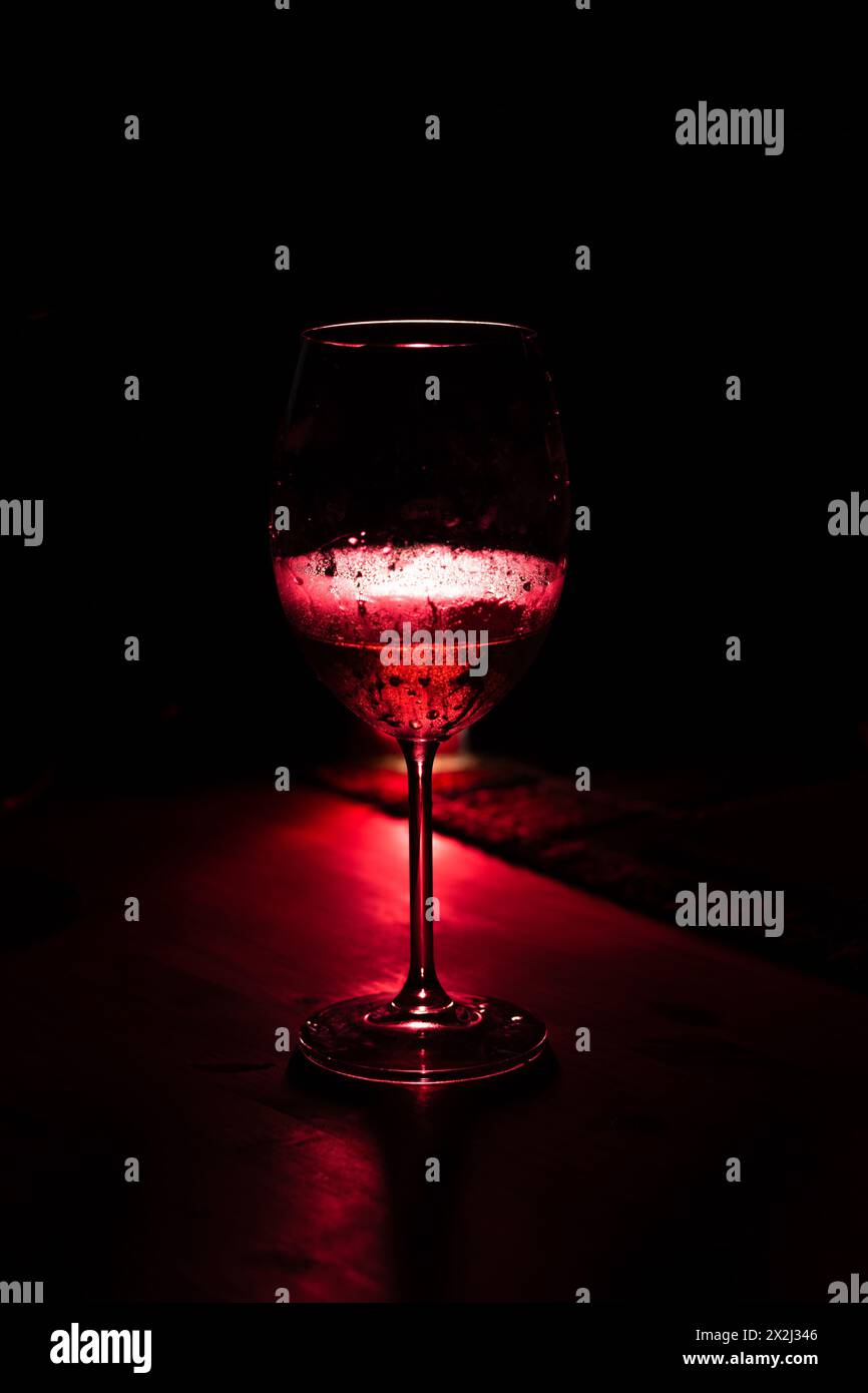 Silhouette di un bicchiere di vino su un tavolo di legno. Luce rossa predominante. Fotografia da bere. Foto Stock