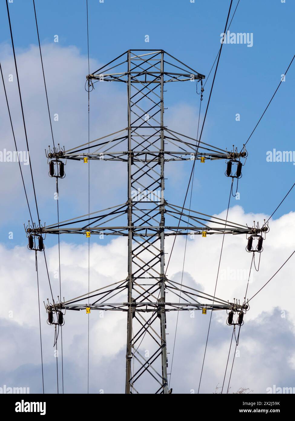 Un polo di trasmissione ad alta tensione con fili e isolanti visibili contro un cielo blu leggermente nuvoloso. Contrassegni di fase visibili. Linee elettriche, strategiche Foto Stock