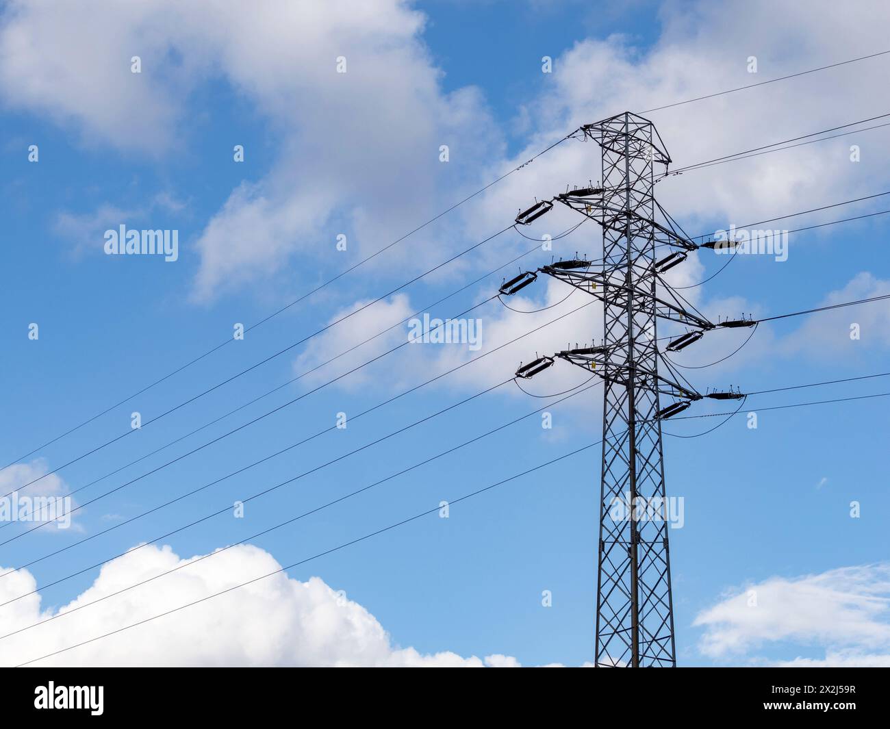 Un polo di trasmissione ad alta tensione con fili e isolanti visibili contro un cielo blu leggermente nuvoloso. Linee elettriche, infrastrutture strategiche. Foto Stock
