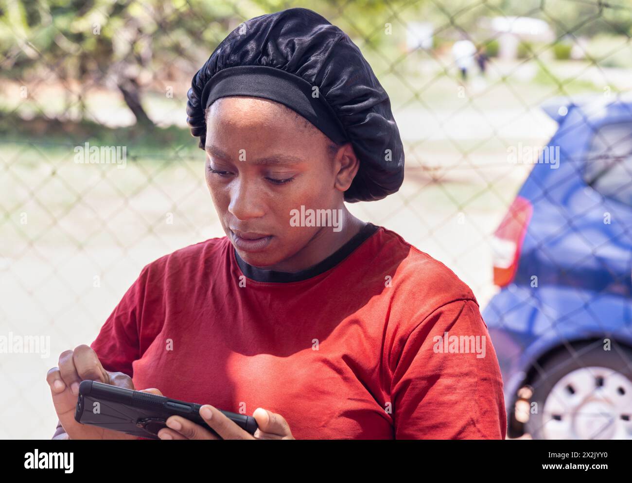 giovane donna africana negoziante che usa uno smartphone di fronte al negozio nella povera cittadina, insediamento informale Foto Stock