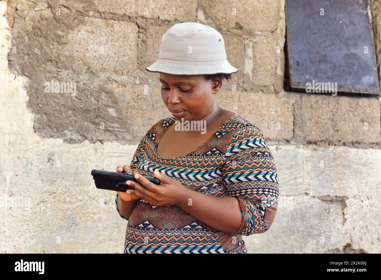 giovane donna africana con un cappello che tiene il cellulare nella povera cittadina, insediamento informale Foto Stock