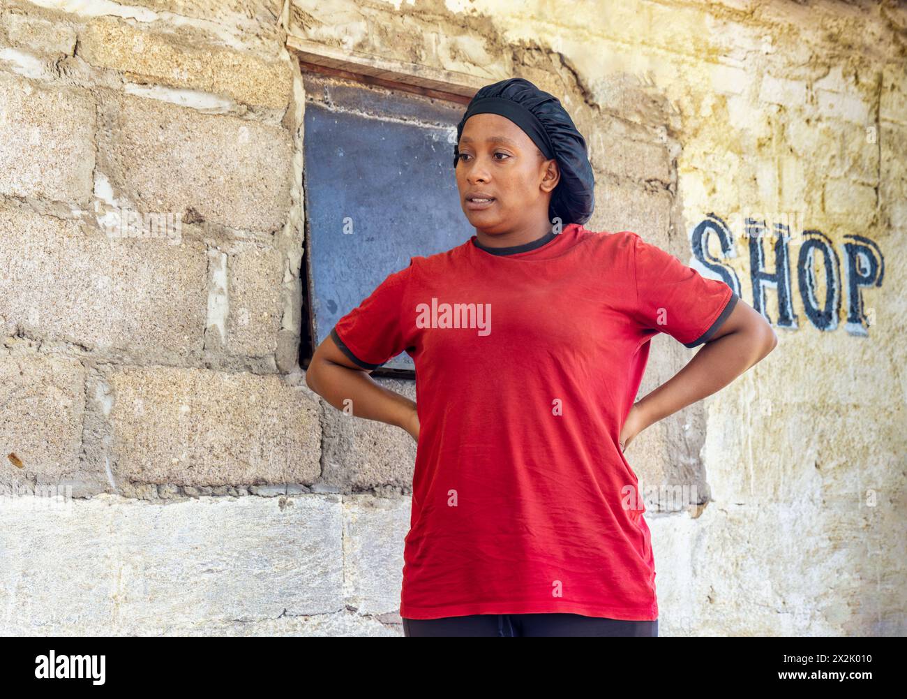 giovane donna africana negoziante in piedi di fronte al negozio nella povera cittadina, insediamento informale Foto Stock