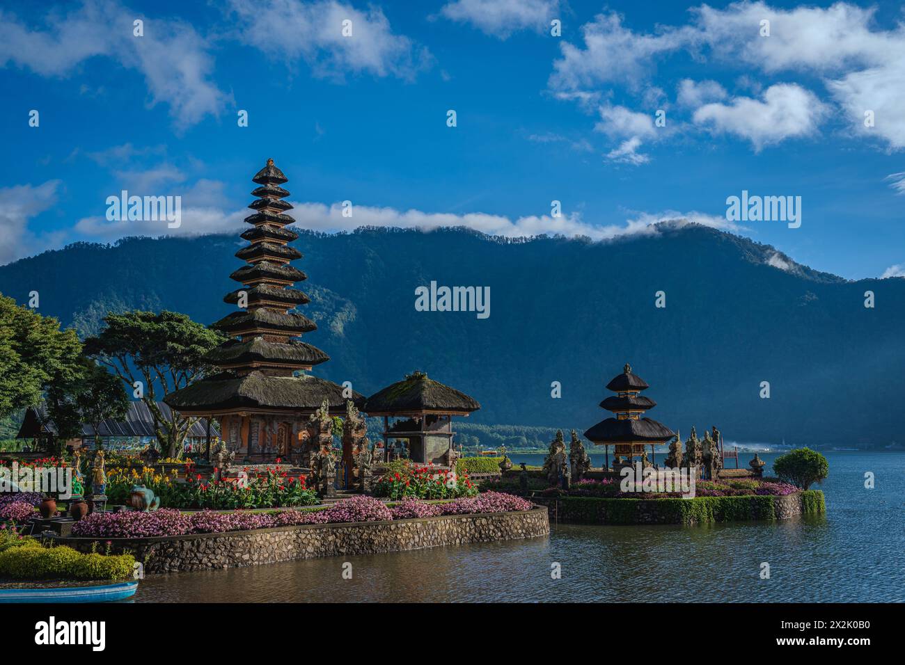 Una vista panoramica di un tradizionale tempio balinese circondato da vividi giardini floreali e adagiato sullo sfondo di una montagna. L'immagine cattura la cultura Foto Stock